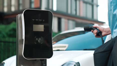 progressive businessman plugs charger plug from charging station to his ev.