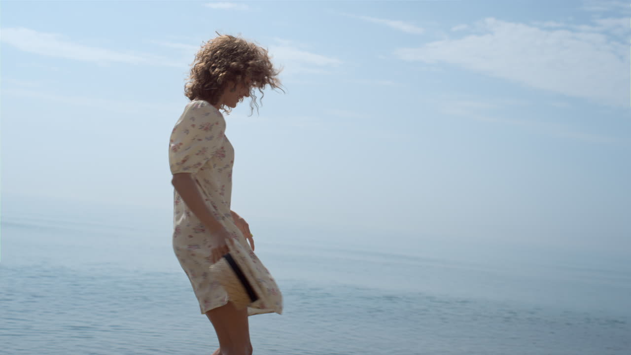 una mujer feliz girando rebotando en la playa de arena húmeda. una chica rizada caminando por las olas del océano.
