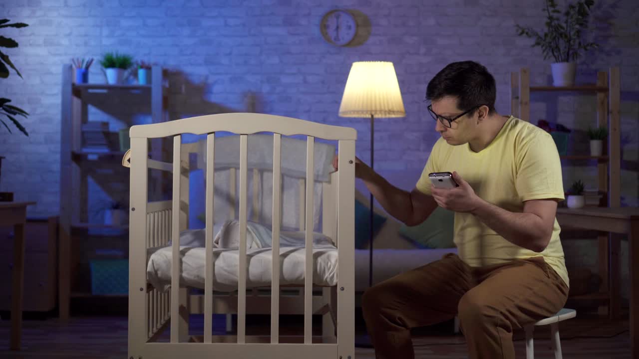 손에 드폰을 들고 있는 독신 아버지가 밤에 아이들의 방에서 인터넷을 검색합니다.