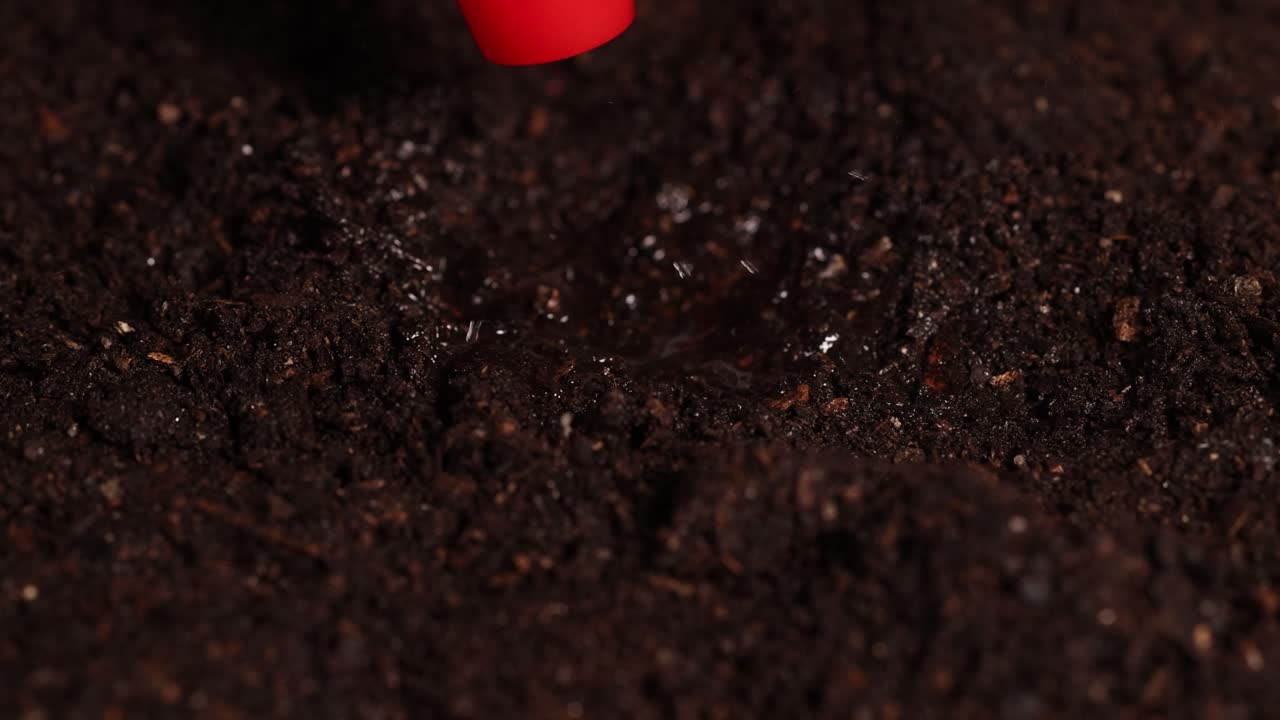 A water droplet impacts soil, creating a mist effect under controlled lighting in a lab setting