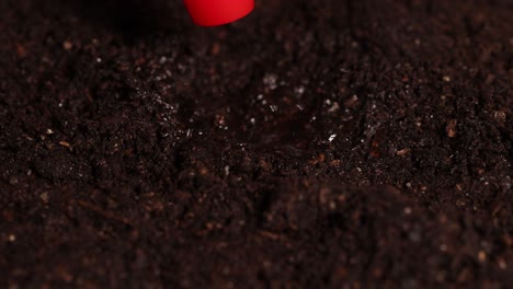 a water droplet impacts soil, creating a mist effect under controlled lighting in a lab setting
