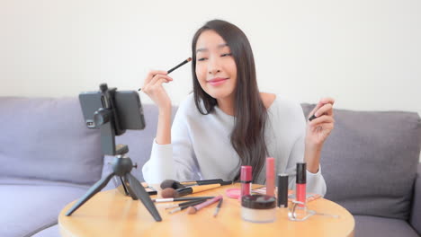 asian female blogger applying makeup mascara with a brush, beauty cosmetics concept makeup youtuber recording video on a smartphone