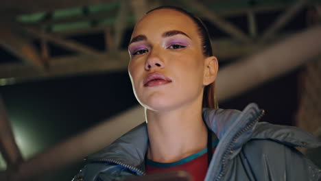 mujer posando ciudad nocturna con teléfono inteligente de cerca. modelo de moda buscando cámara.