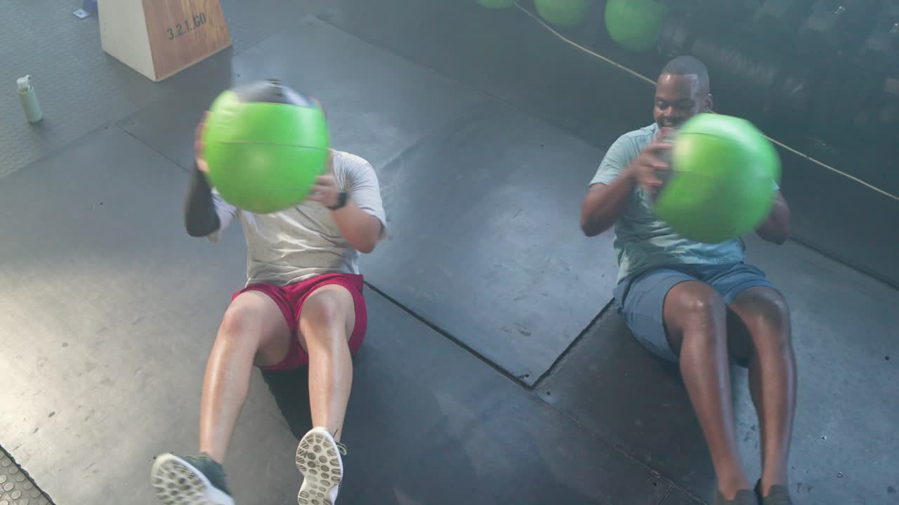 Pria Afrika-Amerika mulai melakukan latihan memutar tubuh di atas matras dengan perlengkapan, mengoper bola hijau untuk membentuk otot perut.