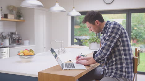 Man-working-from-home-using-laptop-on-kitchen-counter---shot-in-slow-motion