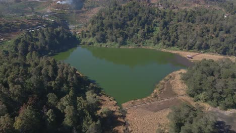 Aerial-view-of-lake-with-green-water-surrounded-by-green-trees