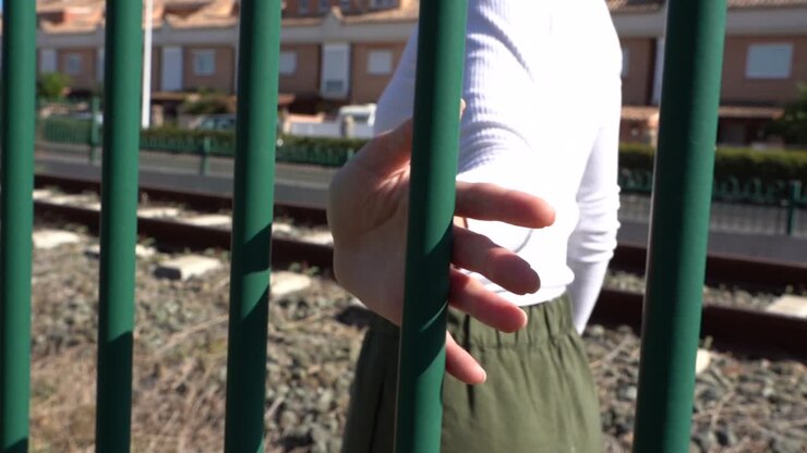 Girl walking and sliding her hand on the railing, in the background houses and train track