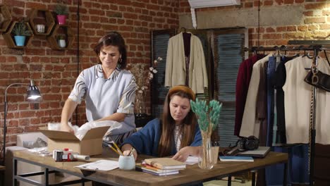 female online shop owners preparing parcel with garment for shipping