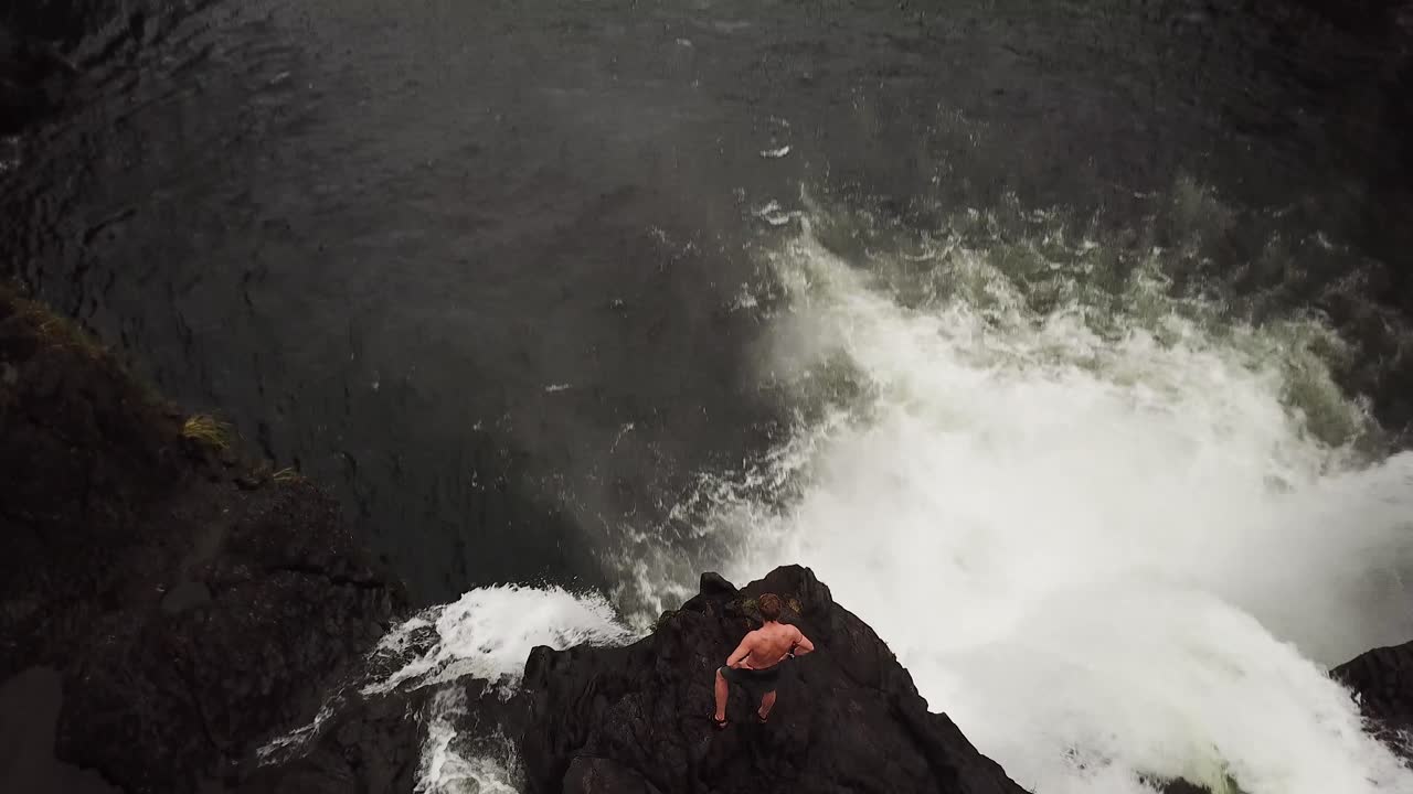 하와이의 거대한 분출 폭포 위에 서서 점프할지 말지 토론하는 남자