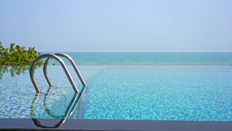 crystal clear water of luxury resort infinity swimming pool with ladder from deep to shallow and blue mosaic tile floor
