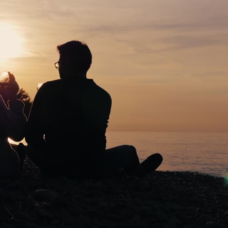 Silhouettes-of-a-young-couple-drinking-wine-at-sunset-on-the-shore-of-the-lake