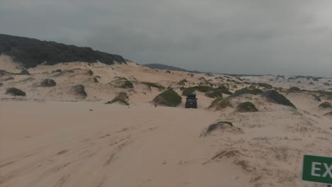 aerial following vehicle driving off sandy beach past exit sign