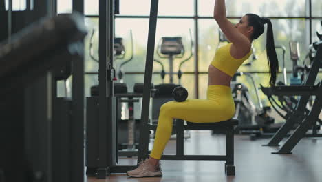 mujer hispana sentada en un simulador en el gimnasio tira de una cuerda de metal con el peso bombea los músculos de la espalda. mujer morena tira del simulador. realizando ejercicio para los músculos de la espalda simulador