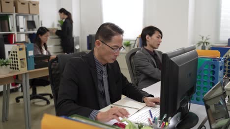 portrait of asian businessman wearing suit is writing notes and doing work on desktop computer with concentration in the office with other colleagues