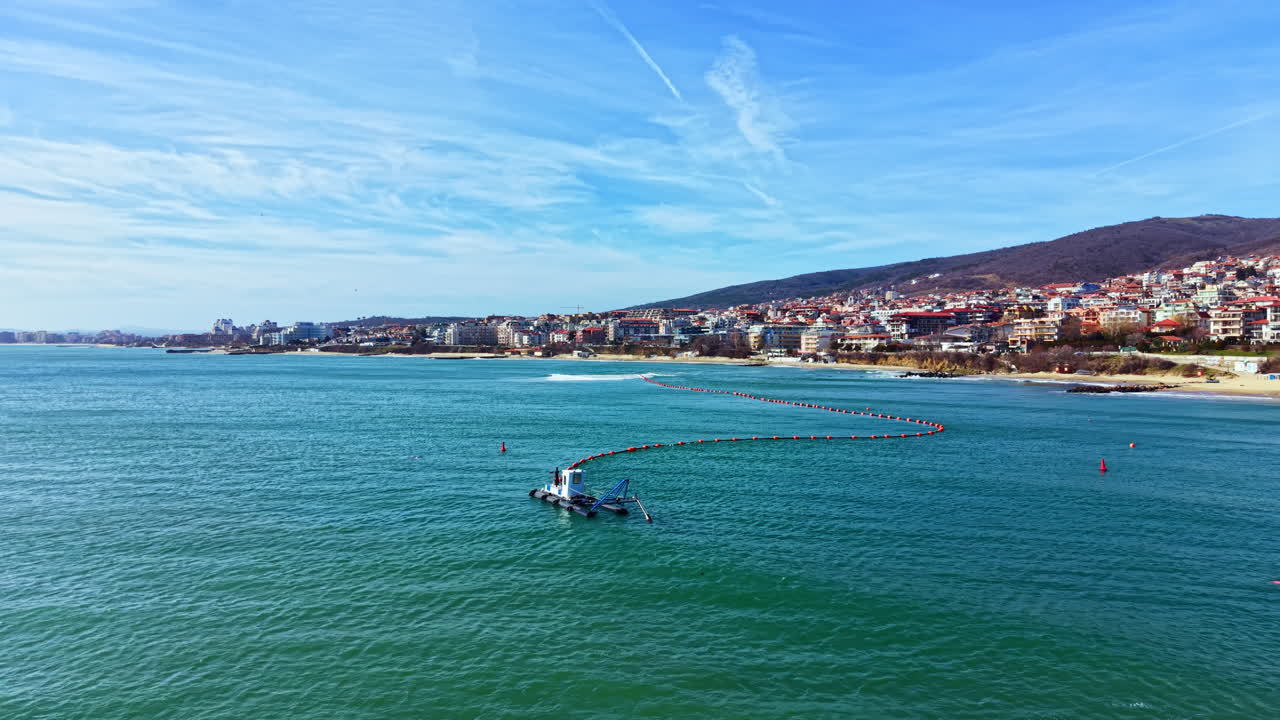 Splendida vista di una barca nell'acqua vicino a una città costiera con edifici e una costa rocciosa, in una giornata limpida d'estate.