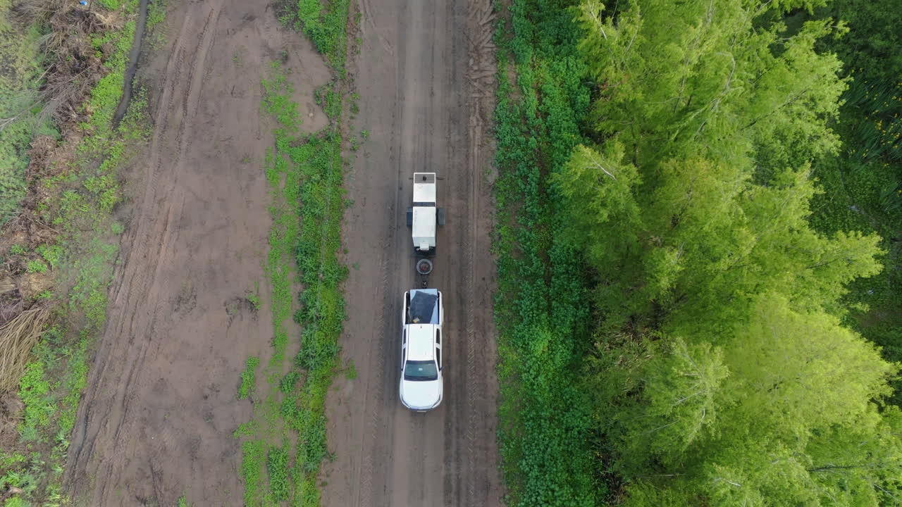 A top-down view shows a car with trailer navigating a dusty sand road. The rough terrain stretches out, emphasizing the vast, open landscape of region as the vehicle moves through the rural scenery.