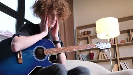 a young curly-haired musician with a guitar plays a calm sad melody. the young guitarist is tired.
