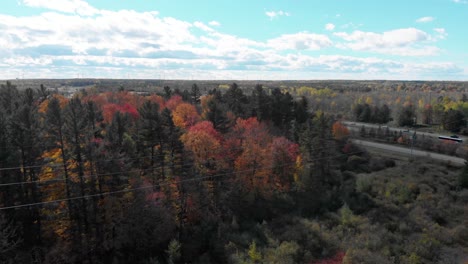 Circling-around-and-then-lower-around-tall-hydro-lines-just-outside-Ottawa,-Ontario-and-then-going-with-them-with-the-autumn-trees-in-the-background-on-a-sunny-day