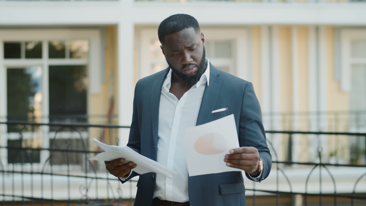 Proud afro business man looking papers outdoors. African guy examining documents