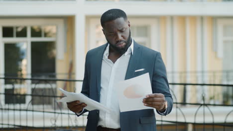 Orgulloso-Hombre-De-Negocios-Afro-Mirando-Papeles-Al-Aire-Libre.-Chico-Africano-Examinando-Documentos