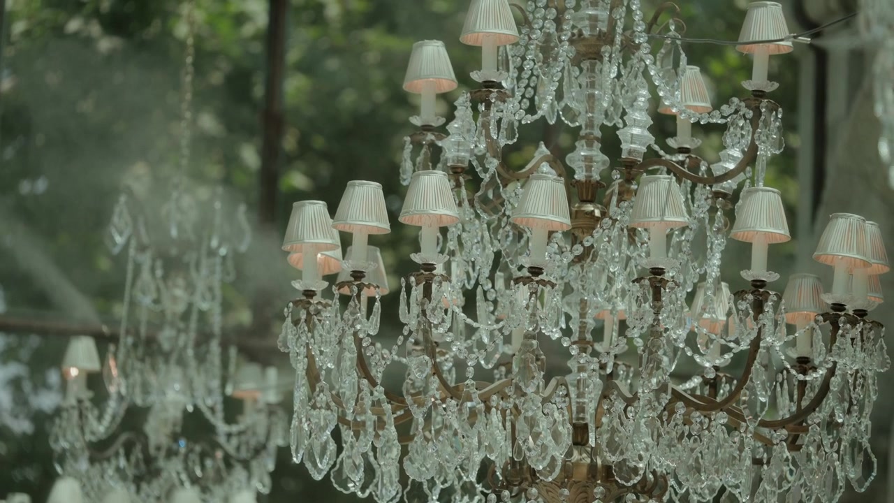 Descrizione: Diversi lampadari di cristallo con paralumi in tessuto appesi in un ambiente da giardino
