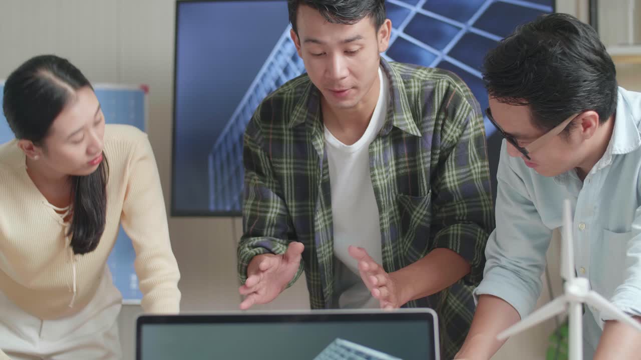 아시아 엔지니어 그룹이 사무실에서 태양전지를 보여주는 노트북을 가진 테이블에서 블루프린트 작업에 대해 논의하고 있습니다.