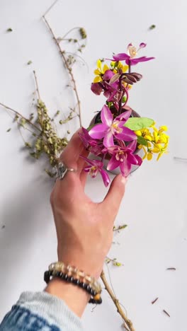 hand holding a floral arrangement with orchids and branches