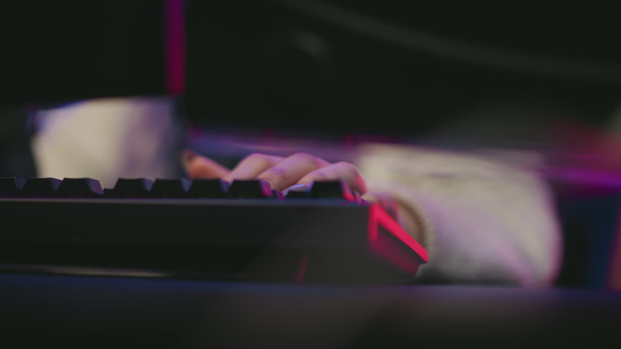 female hand with glossy manicure typing on backlit mechanical keyboard seen through narrow gap between dark monitor screens in moody neon studio, focus on polished nails and tech interaction