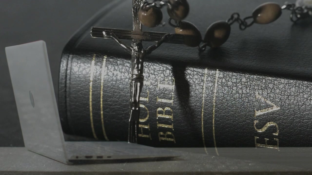 Ciondolo a crocifisso di metallo che entra dall'alto, scende e oscilla, posizionandosi sulla Sacra Bibbia