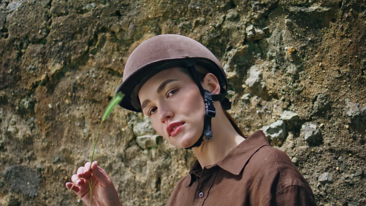 Equestrian woman holding spikelet looking camera portrait. Woman posing wall