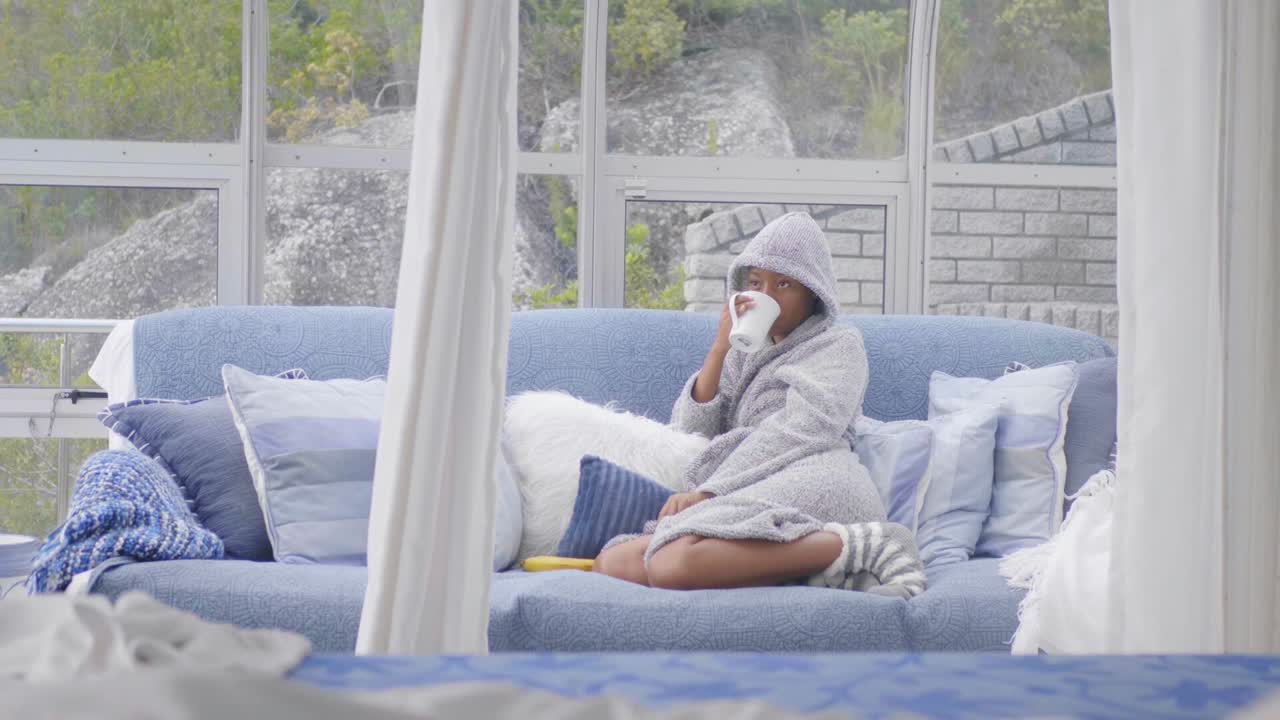 편안한 소파에 앉아 차를 마시는 젊은 아프리카 여성