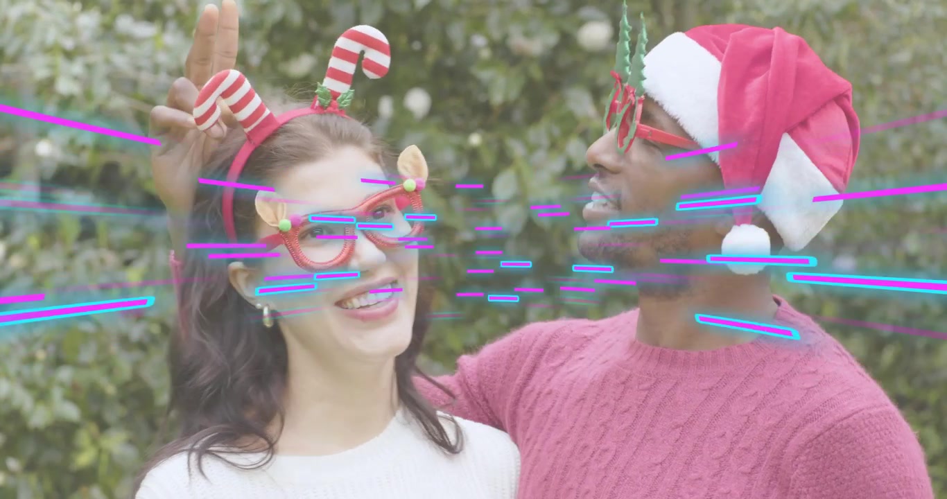 Couple filming holiday ad woman reaching up adjusting Santa hat, man aligning antlers