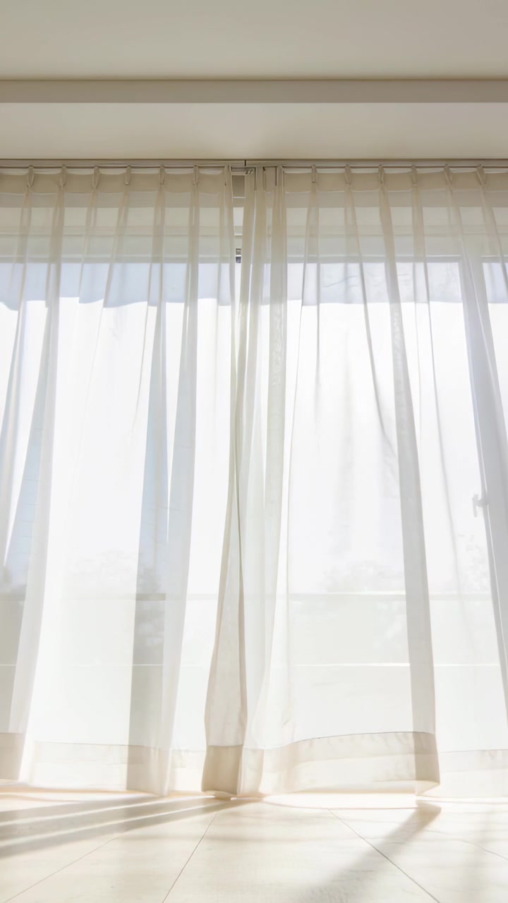 Video vertical: Cortinas transparentes ondeando suavemente con la brisa, deslizándose sobre el suelo de baldosas junto a una puerta de cristal.