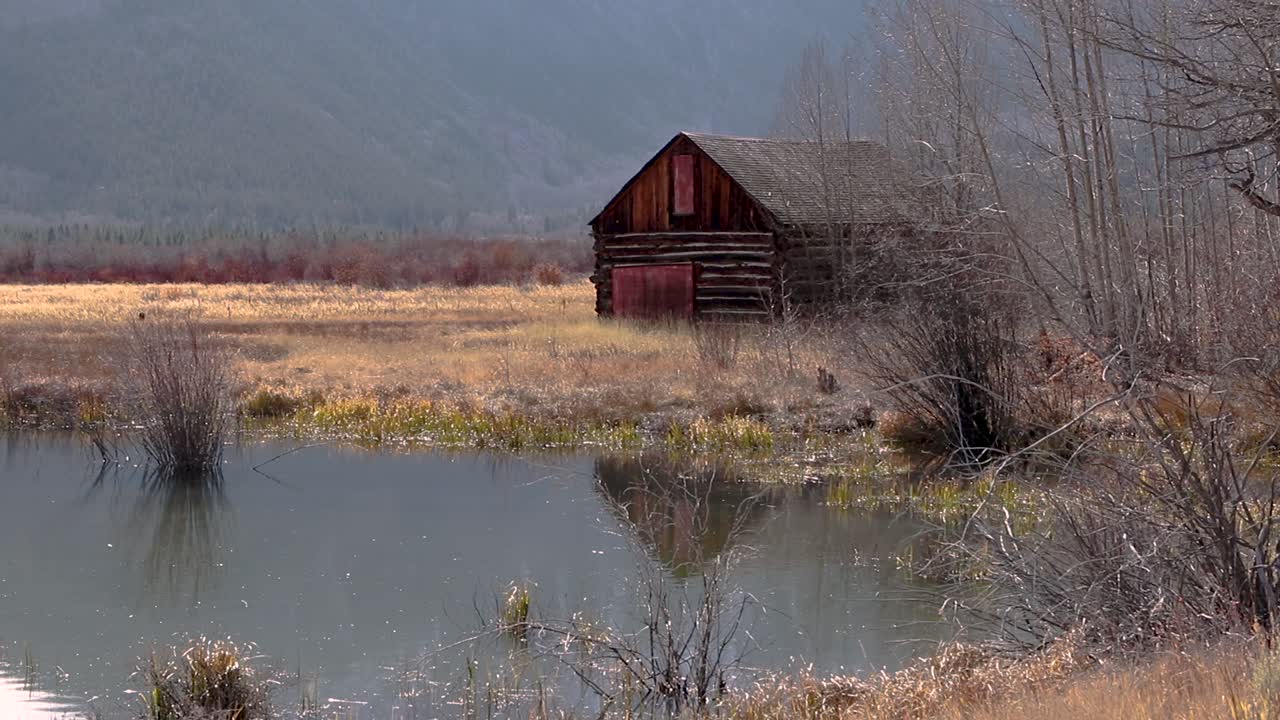 Slight upward panning motion showing rustic cabin in idyllic mountain scene overlooking a small pond