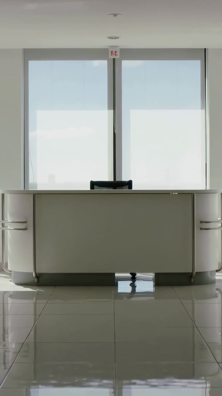 Video verticale: Telecamera che si muove lentamente mostrando scrivania e sedia nella hall con riflessi dalle finestre.