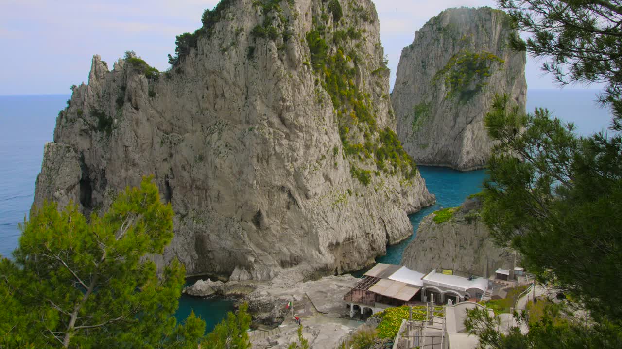 con vistas a las rocas farallones, la costa y el mar con agua azul y casas al fondo en capri, italia