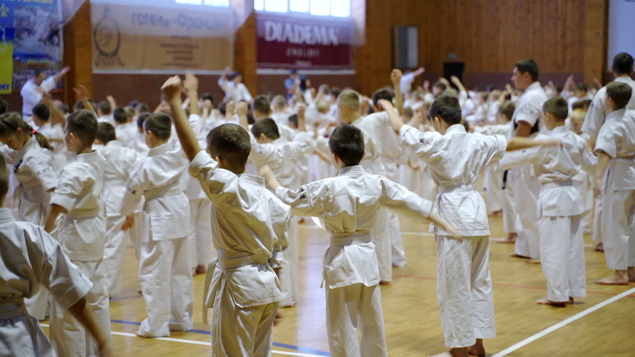 Teenage athletes wearing white kimonos doing exercises. Older masters walk between young sportsmen for control.