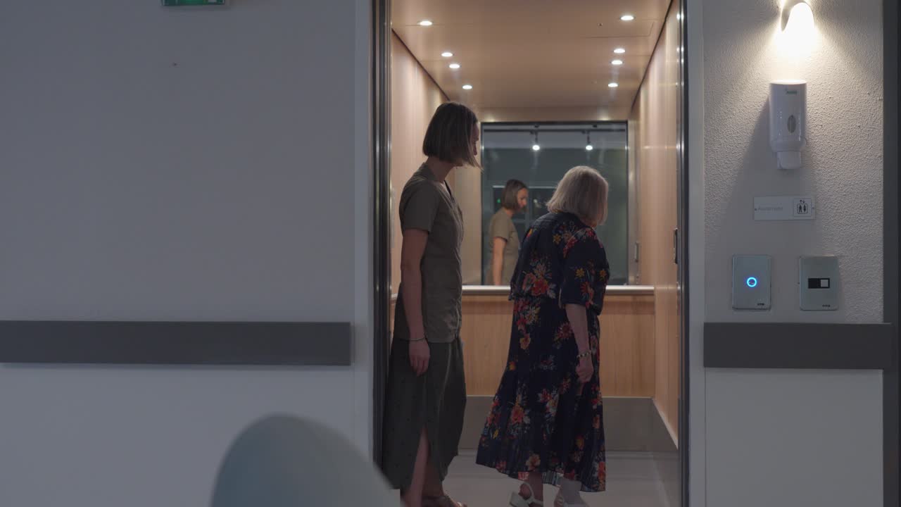 요양원에서 노인 여성이 엘리베이터를 이용하는 데 도움을 주는 조수, 그녀는 바닥을 선택합니다.