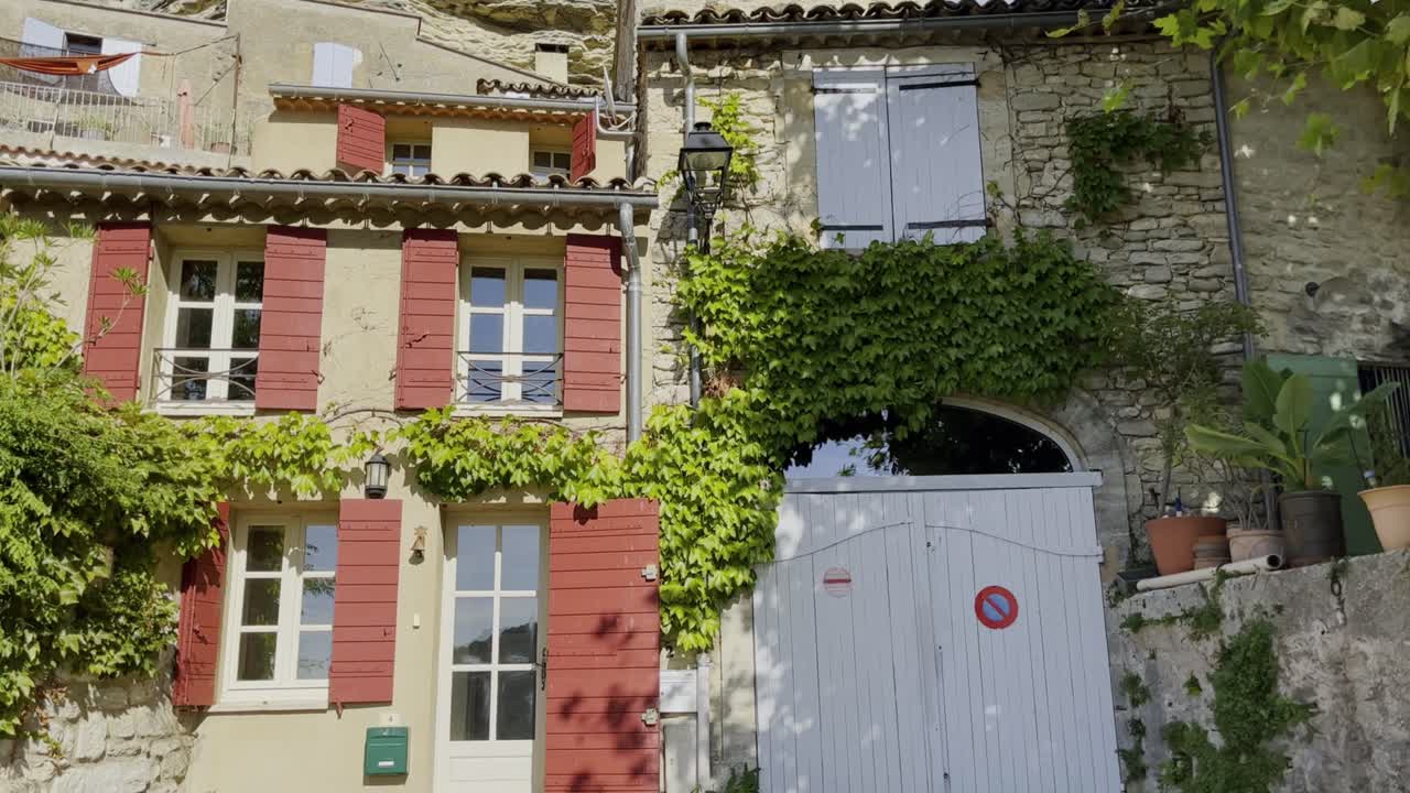 Piccola casa francese con belle finestre ai piedi di una collina con un'altra casa, alcune piante e una grande roccia sullo sfondo con bel tempo
