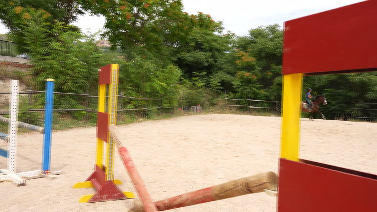 Woman riding a horse quickly around a track with hurdles for training. Slow motion