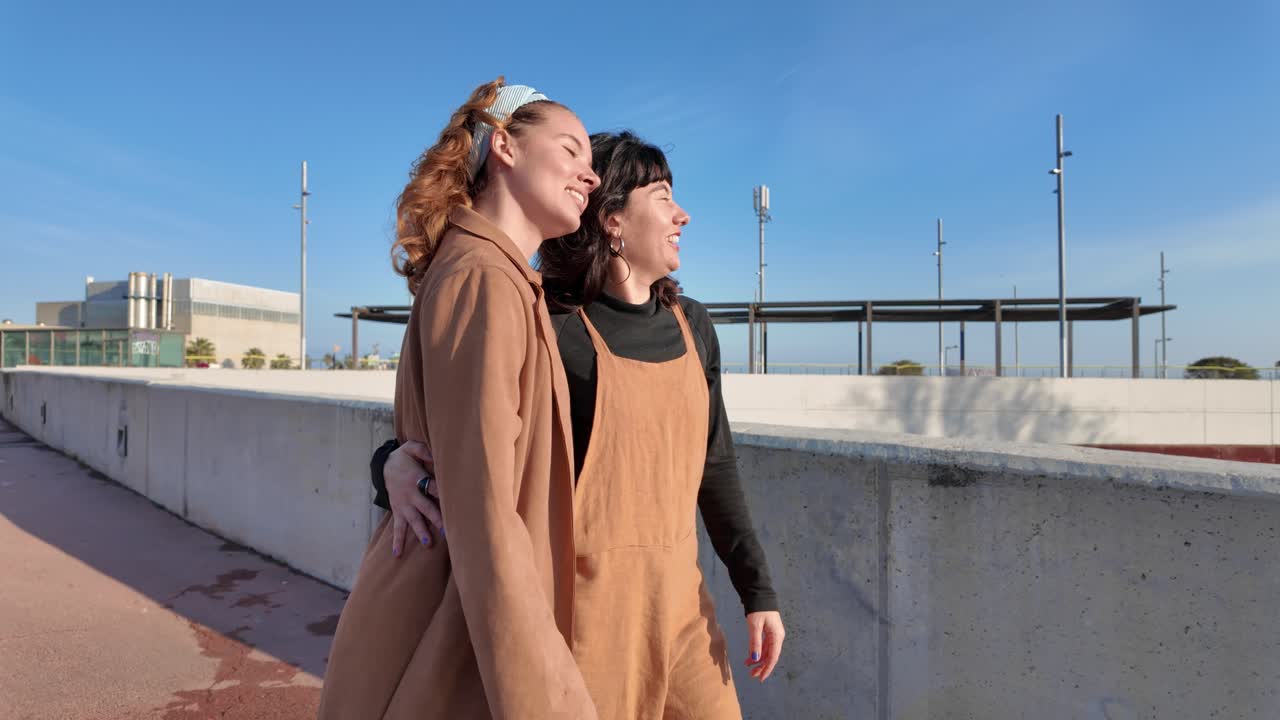 Two smiling women embrace in an urban setting on a sunny day