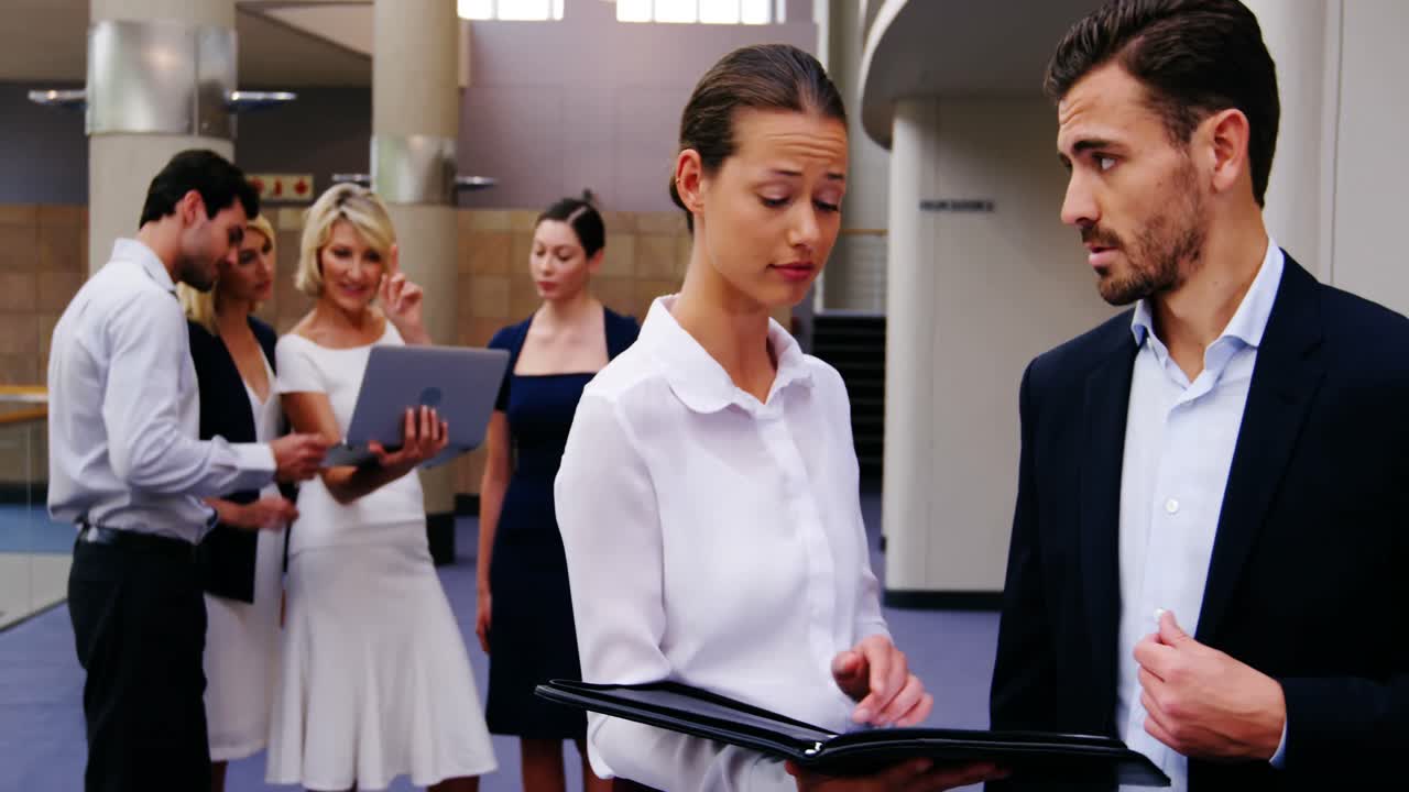 Business executives discussing over file while colleagues interacting in background