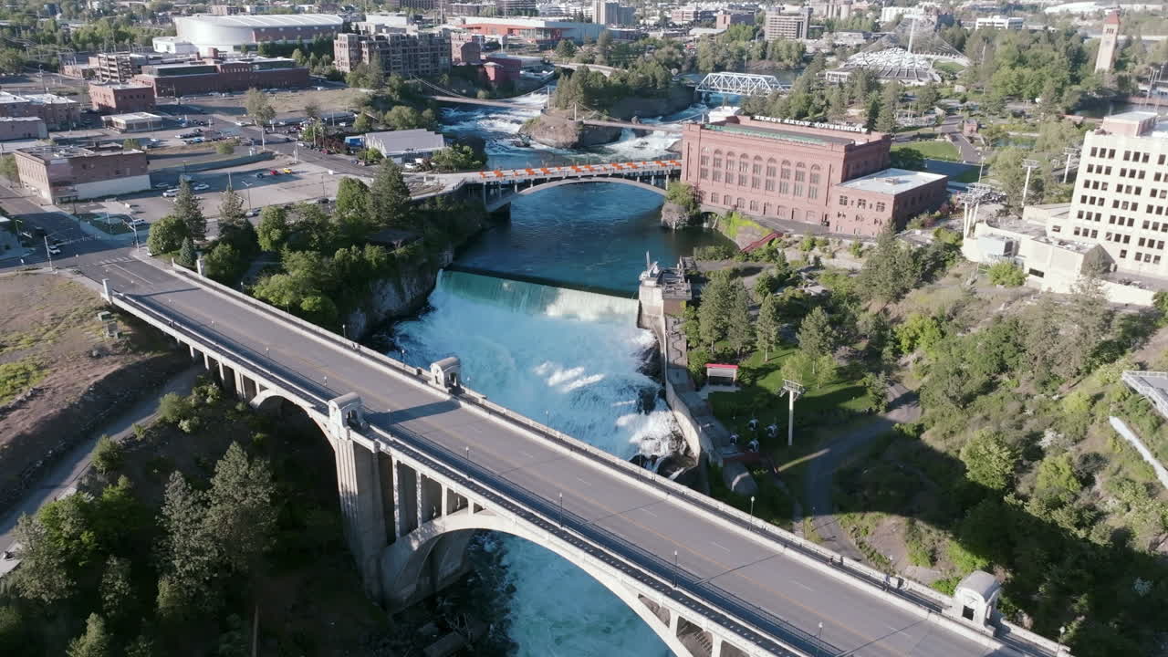 An aerial view of Spokane Falls cascading beneath a series of bridges, framed by the historic red brick Washington Water Power building and downtown Spokane