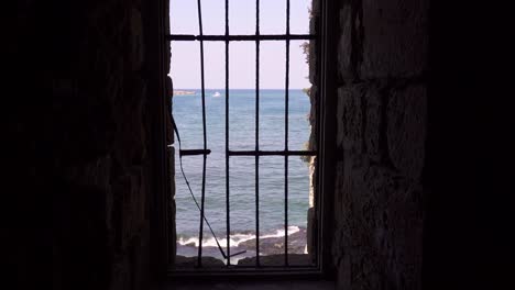 Edificio-Abandonado-Con-Ventana-Rota-Enrejada-Sobre-El-Mar-Ondulado