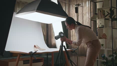 asian female photographer talking on smartphone while taking photos of women's shoes in home studio