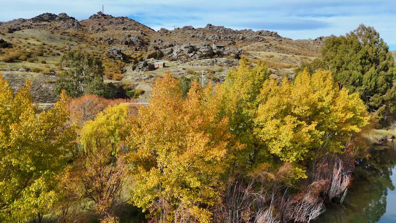 Drone captures vibrant autumn foliage and rugged terrain in Cromwell, New Zealand. Bright colors and serene atmosphere highlight natural beauty