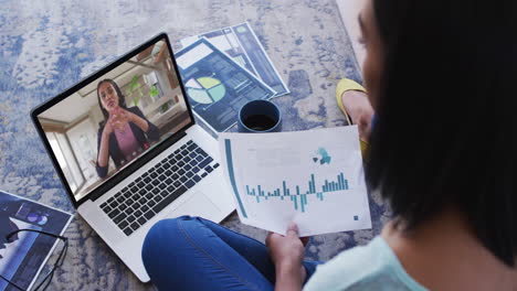 African-american-woman-holding-a-document-having-a-video-call-on-laptop-at-home