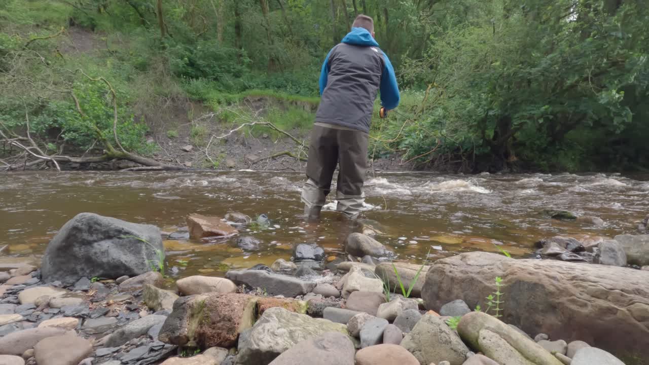 disparo estático bajo de un hombre vadeando y pescando con mosca en un pequeño río aislado en escocia