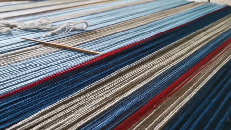 multicolor wool threads in closeup on a weaving board with weaving needle, pan left