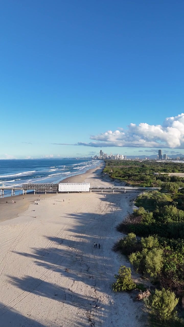 Dron captura una playa serena y el perfil urbano en Gold Coast, Australia, bajo cielos azules despejados con olas suaves